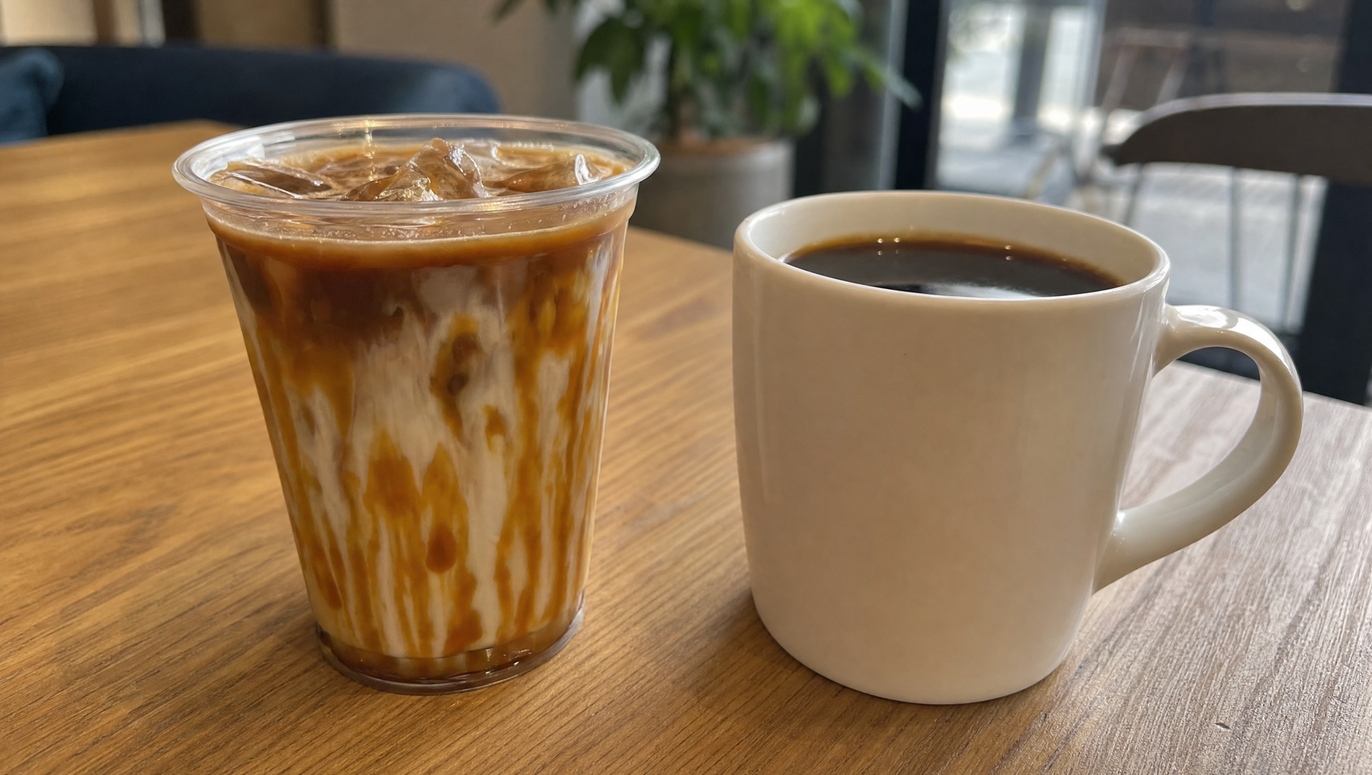 An iced caramel coffee beside a plain black coffee on a wooden table — two very different orders